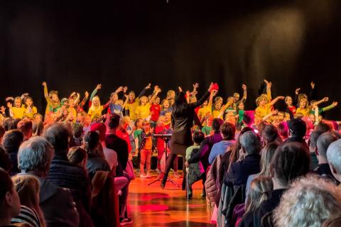 Der Kinderchor Smallbird singt vor Publikum und macht eine ausschweifende Armbewegung