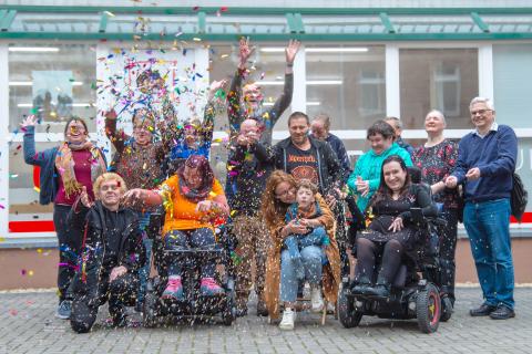 Gruppenbild des Festivalbeirats vom Schranken Los-Festival: Mehrere Menschen verschiedenen Alters und Geschlechts, mit verschiedenen Behinderungen werfen Konfetti in die Luft und jubeln